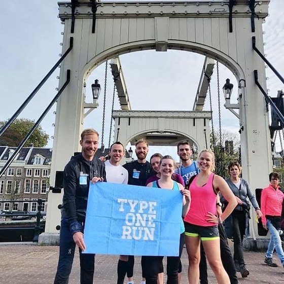 A group of runners holding a blue Type One Run banner on a historic bridge in Amsterdam